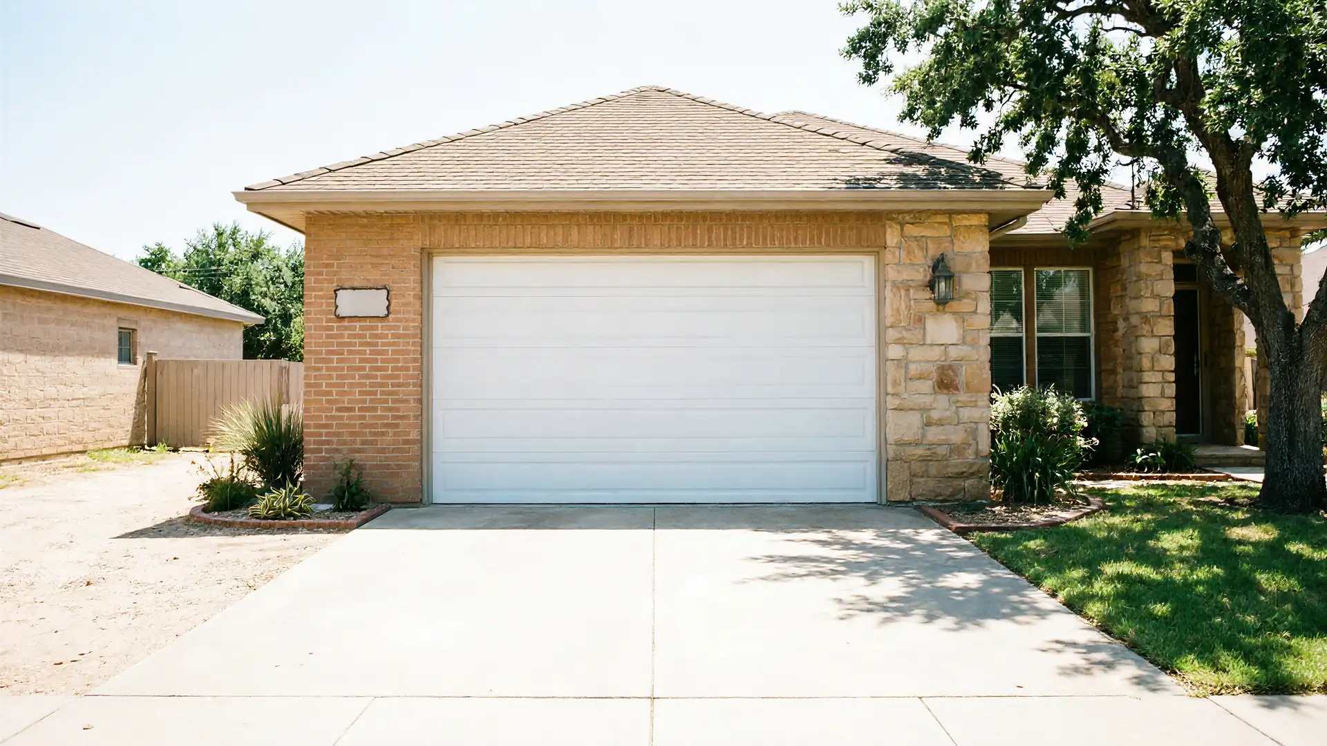 A white garage door is on a brick and stone house with a tree.